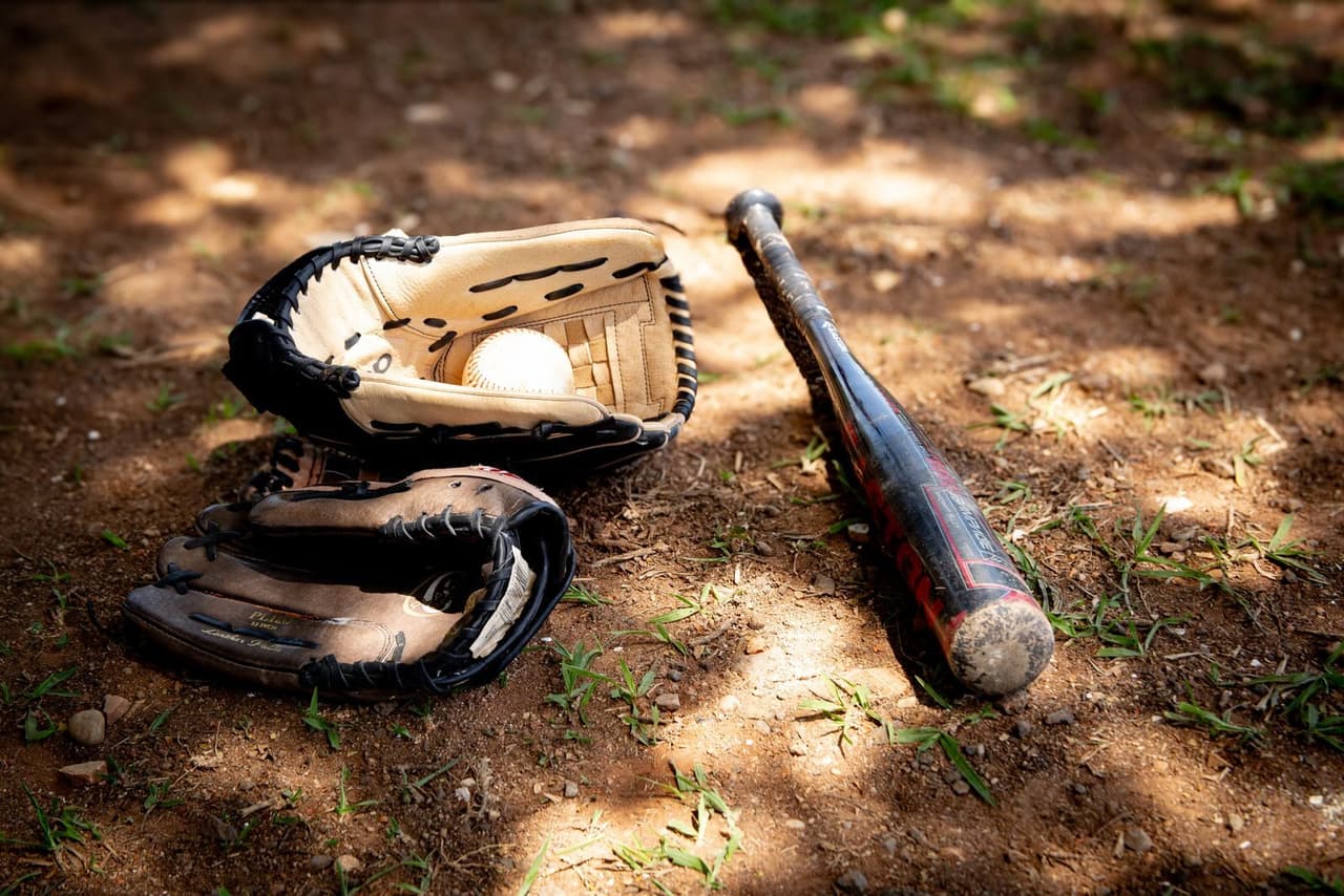 A baseball bat, glove, and ball resting on the infield dirt