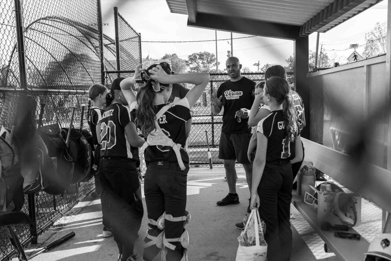 A youth softball coach talking with players in the dugout during a game