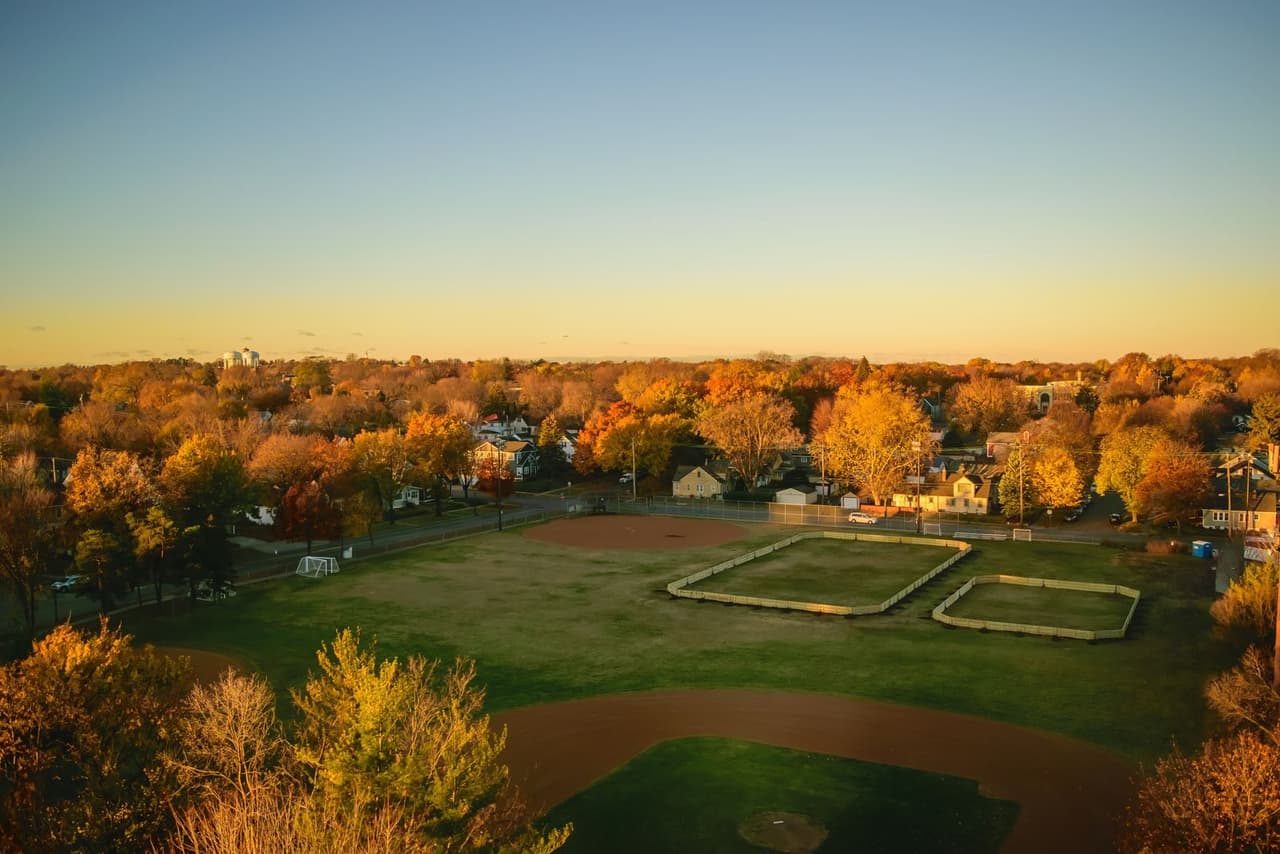 A youth baseball field surrounded by trees in full autumn color at golden hour