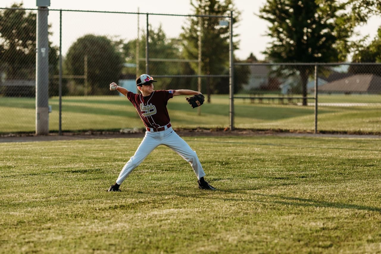 A youth baseball player in a maroon jersey mid-throwing motion on a grass field