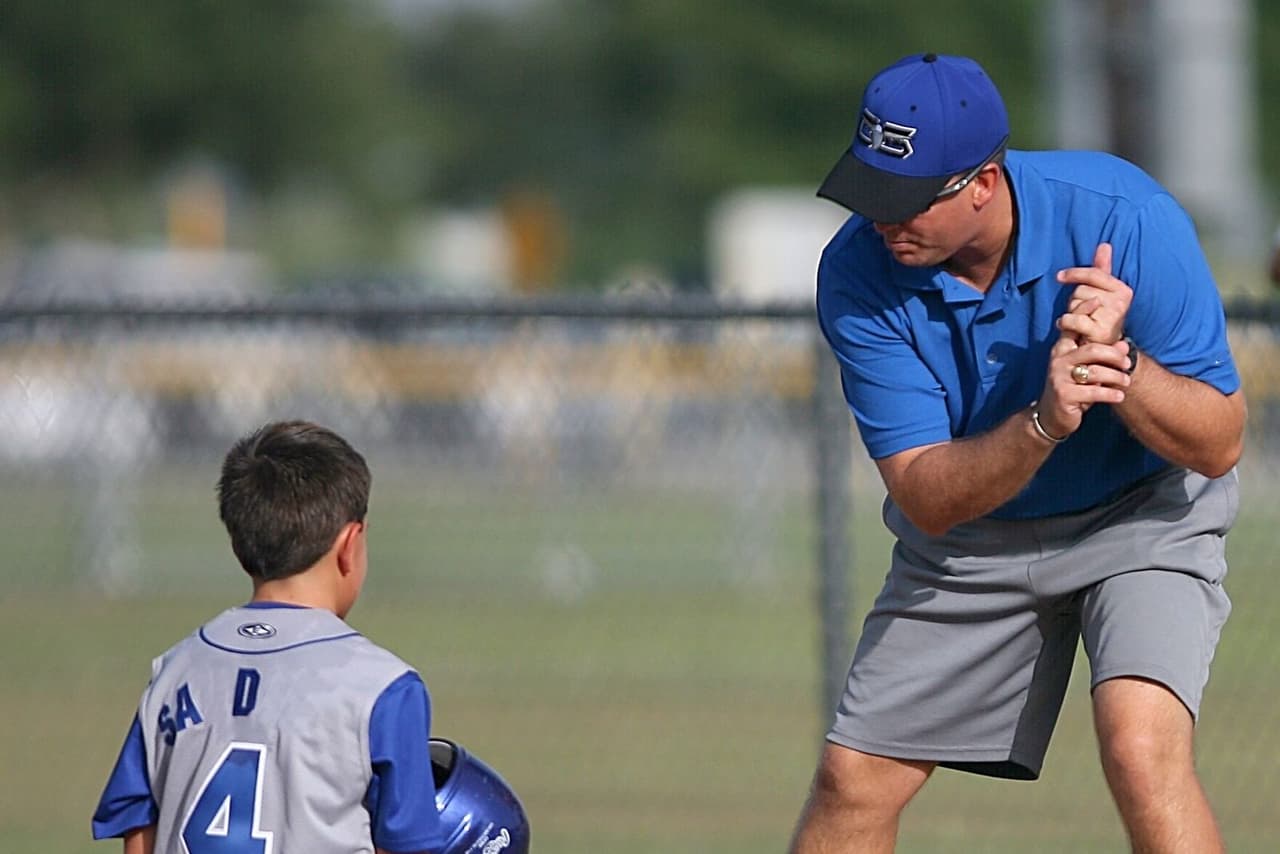 Youth baseball coach kneeling to instruct a young player on the field