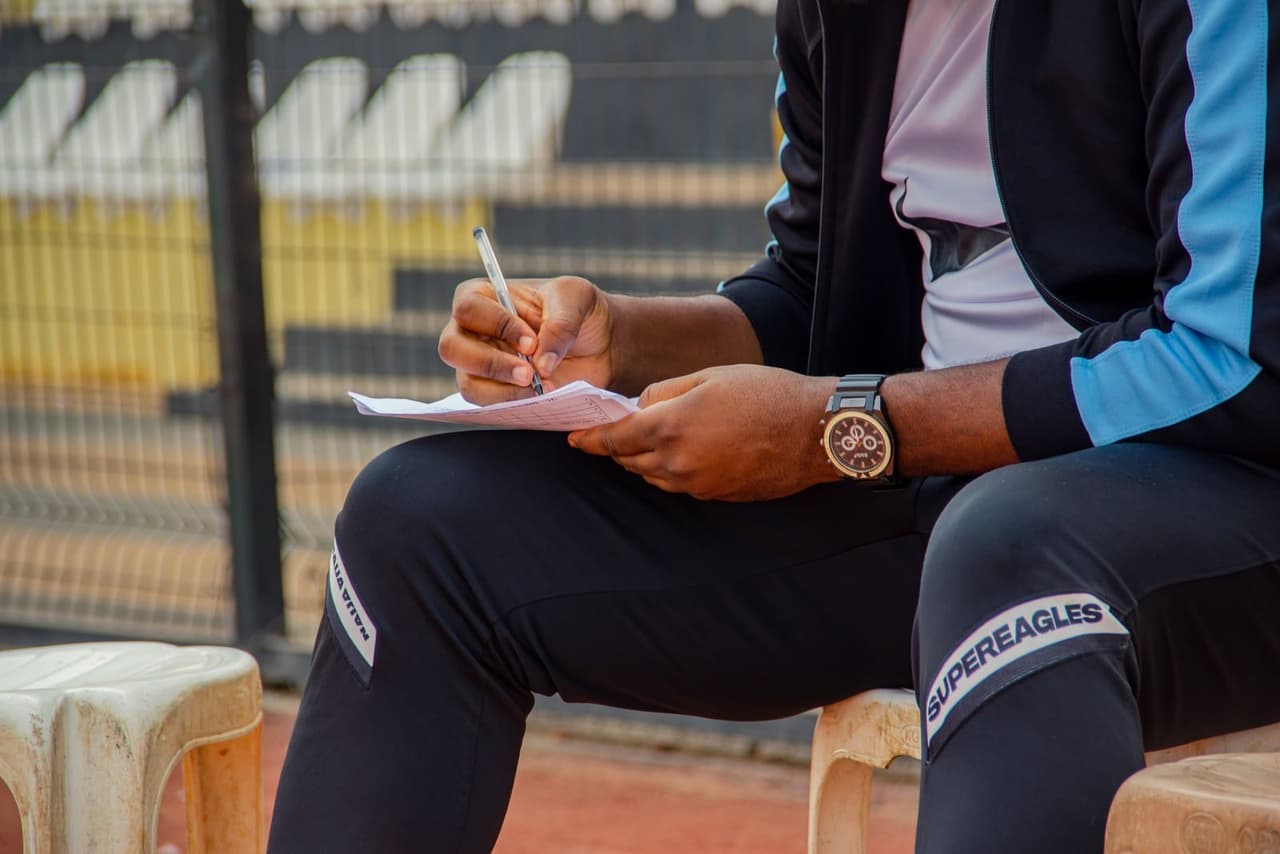 A coach sitting in the dugout writing notes on a pad during a game