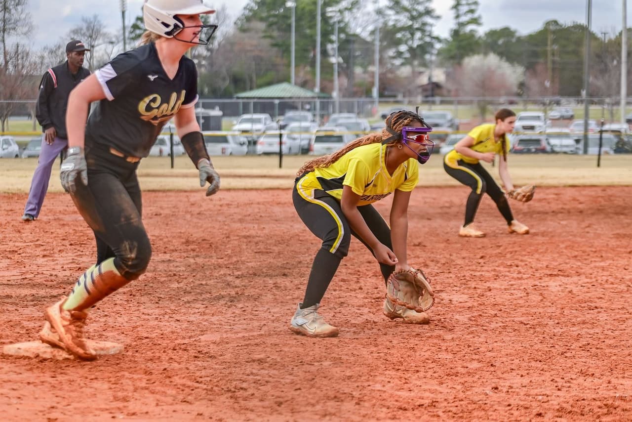 Softball infielder in a low ready position with a runner standing on the base beside her