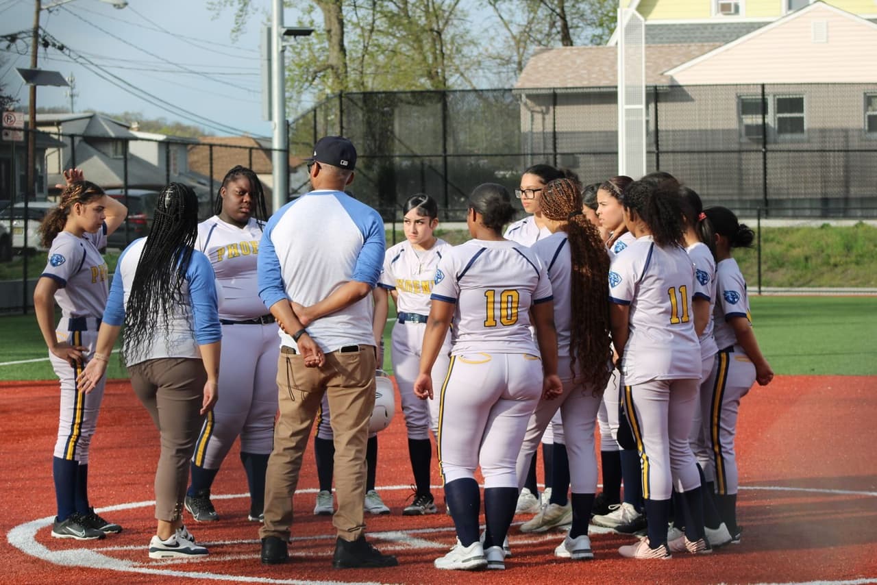 Softball coach standing with his players gathered around him in the pitching circle before a game