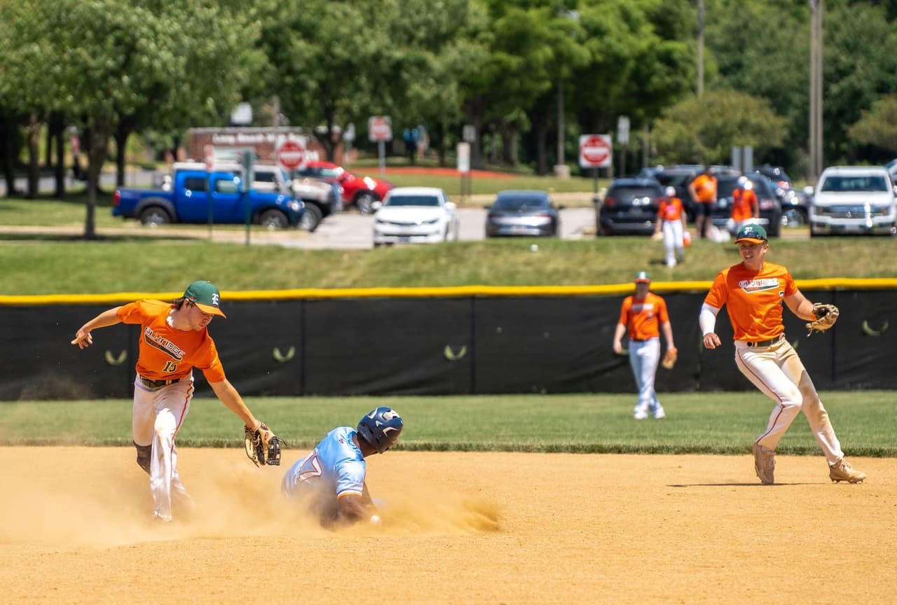 Teenage shortstop applying a tag at second base as a runner slides in, with the second baseman backing up the play