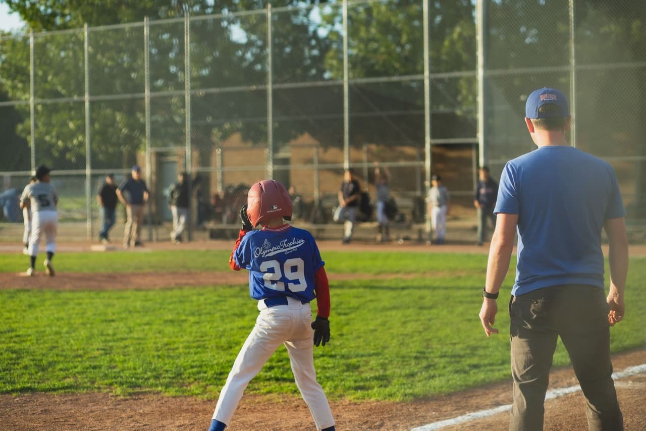 Youth baseball coach watching a young player take a lead off base during a game