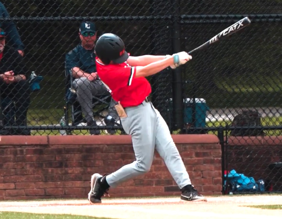 Youth baseball player in the on-deck circle near the dugout exit with helmet on and bat ready, waiting for their turn to hit
