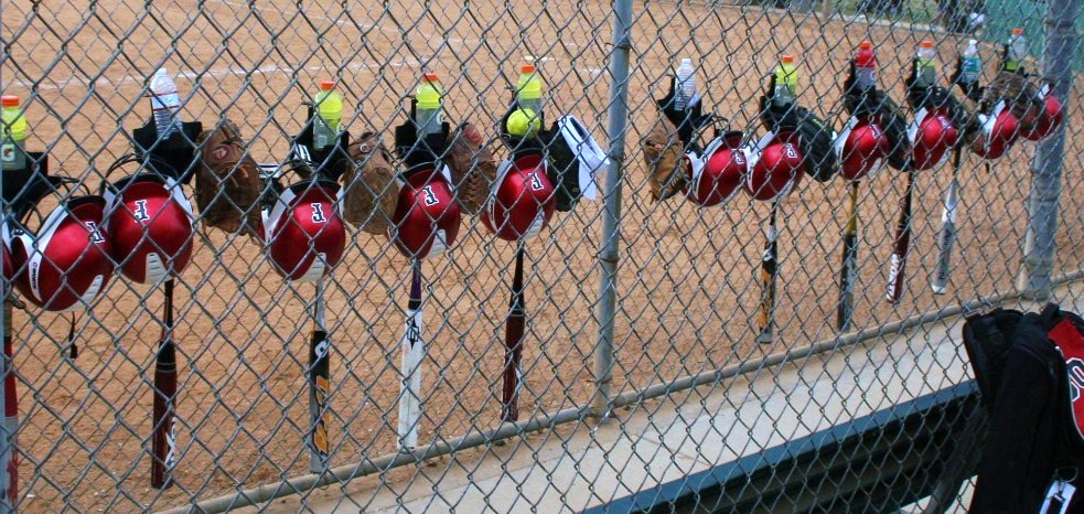 Well-organized youth baseball dugout with helmets on fence hooks, bats in a rack, and gear bags stored neatly under the bench