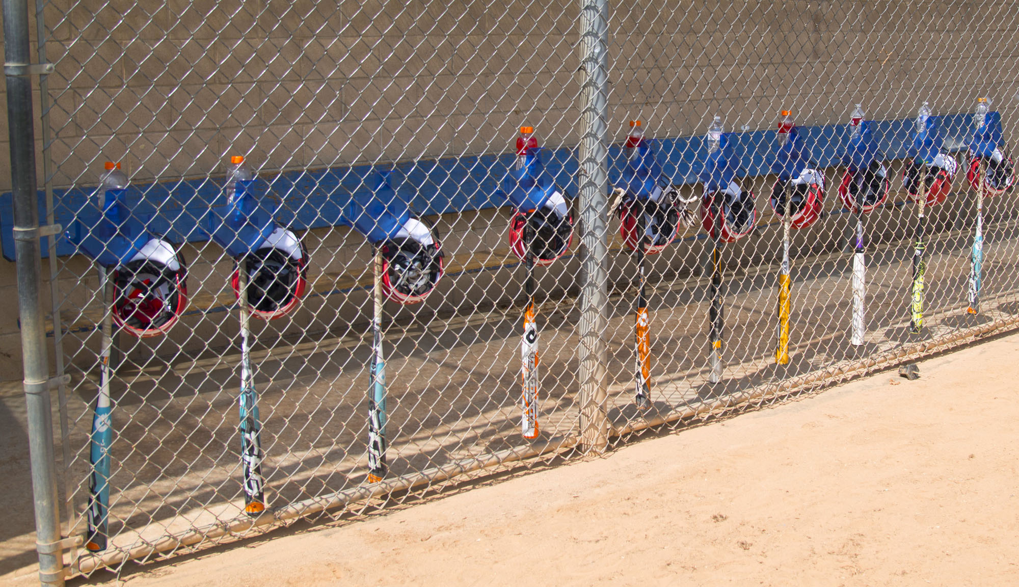 Travel baseball team portable dugout setup at a tournament field with hanging organizer, bat rack, and lineup board on the fence