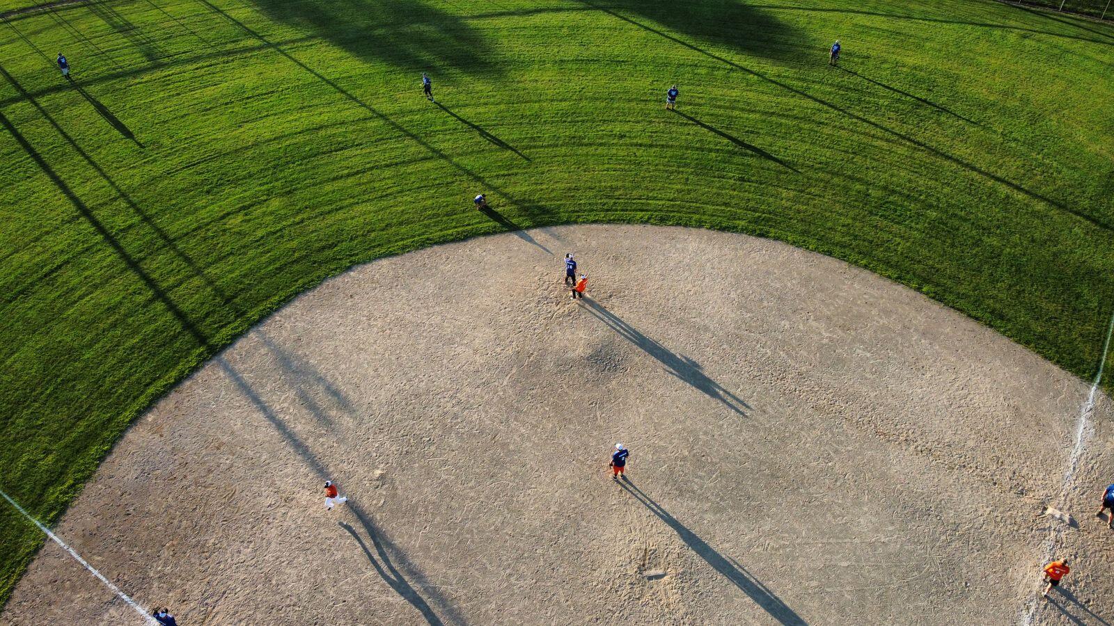 Aerial view of a baseball infield in late afternoon light with players spread across the dirt and grass