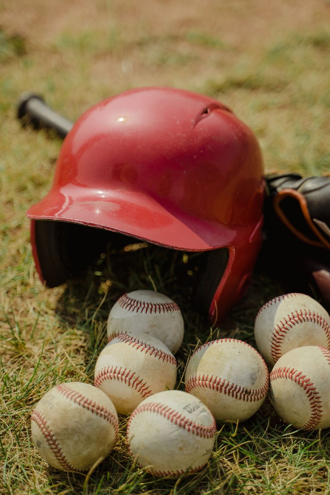 Baseball helmet, glove, and balls laid out on the grass before practice