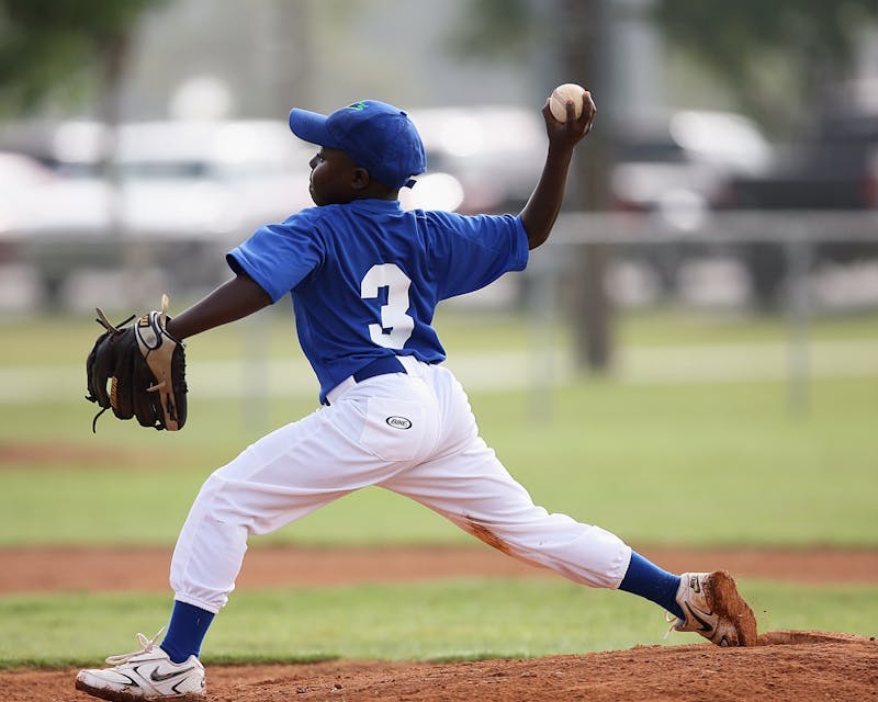 Youth baseball player in throwing motion during long toss arm warmup on a grass field before practice