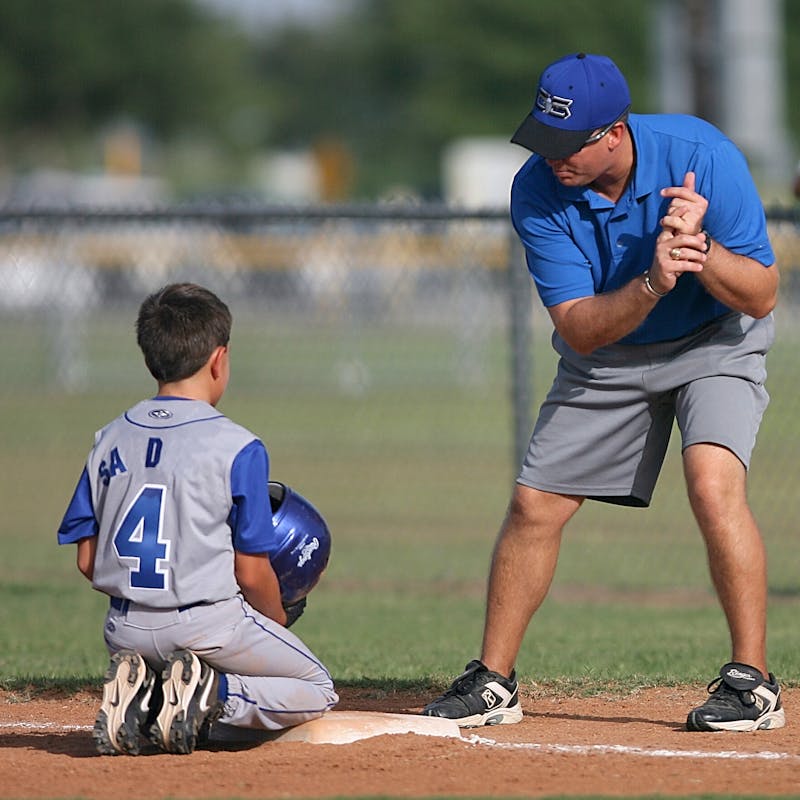 Youth baseball coach holding a clipboard reviewing the practice warmup plan with players standing in a line on the field
